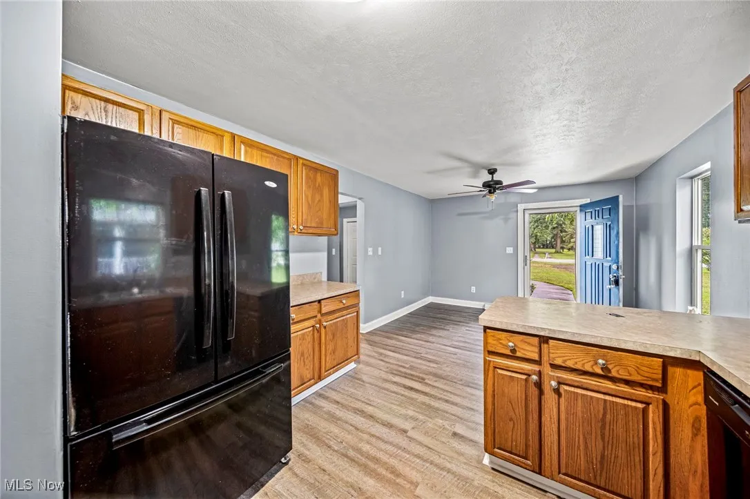 Kitchen featuring black appliances, light wood-style floors, a textured ceiling, light countertops, and brown cabinetry