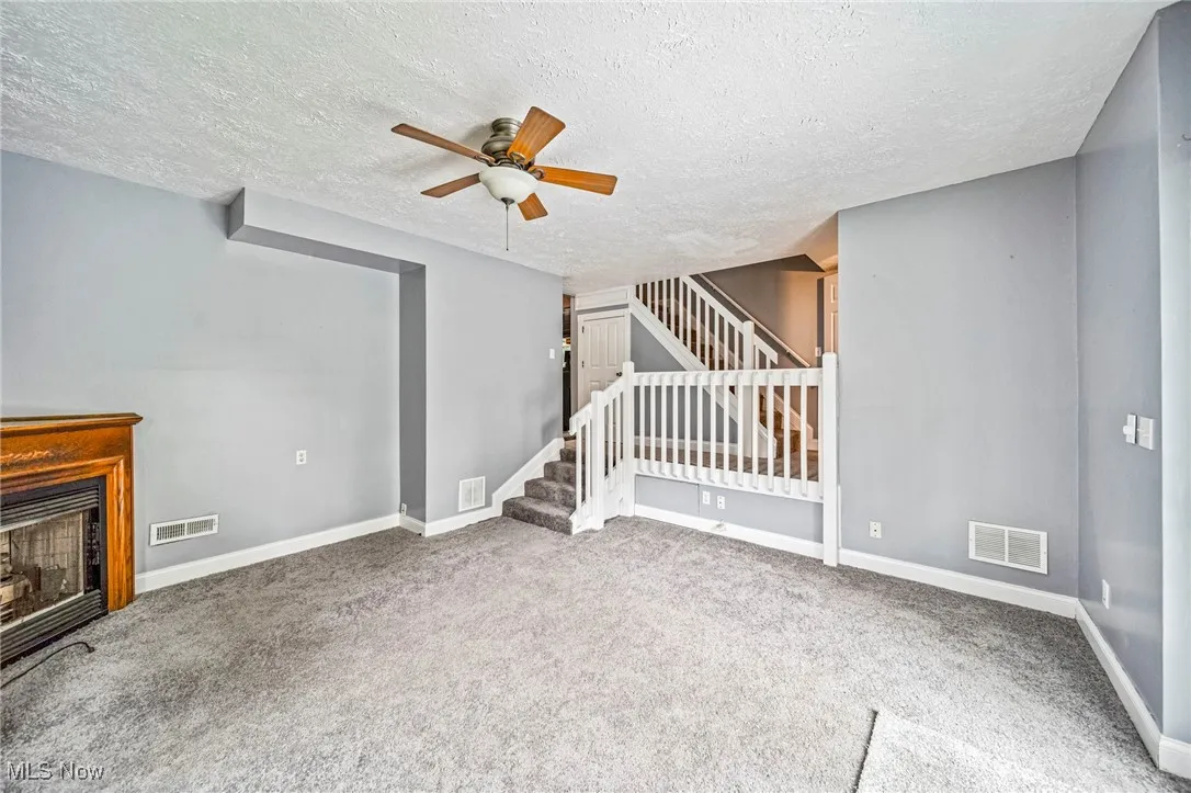 Unfurnished living room with carpet flooring, a textured ceiling, a ceiling fan, a fireplace, and stairway
