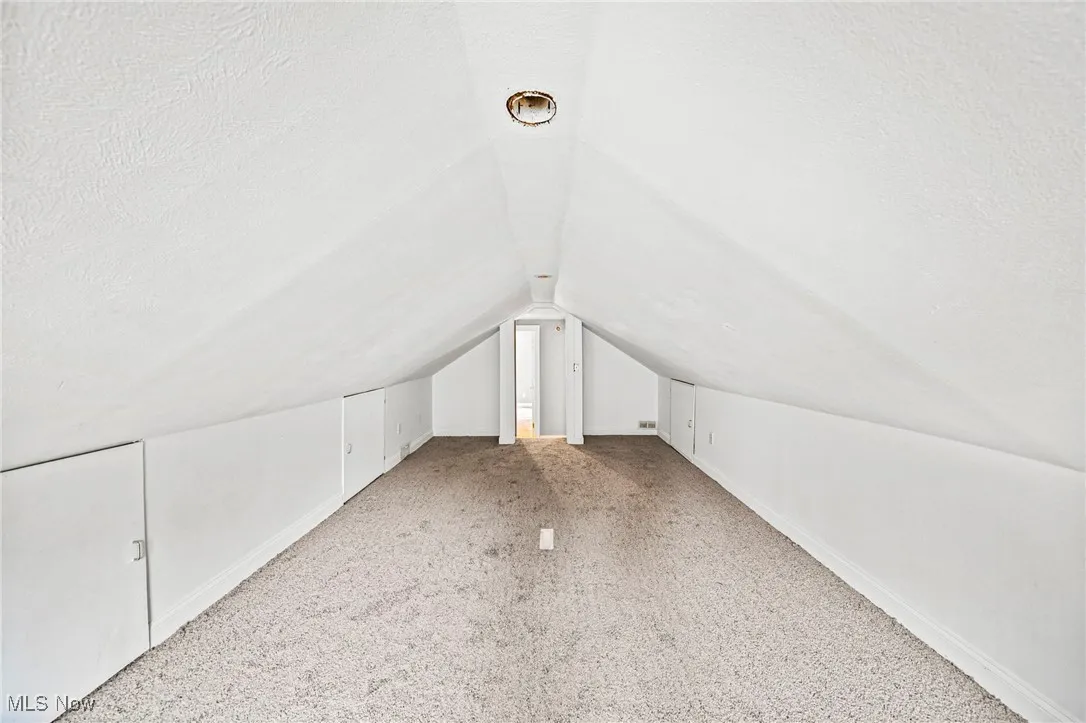 Additional living space featuring vaulted ceiling, a textured ceiling, and light carpet