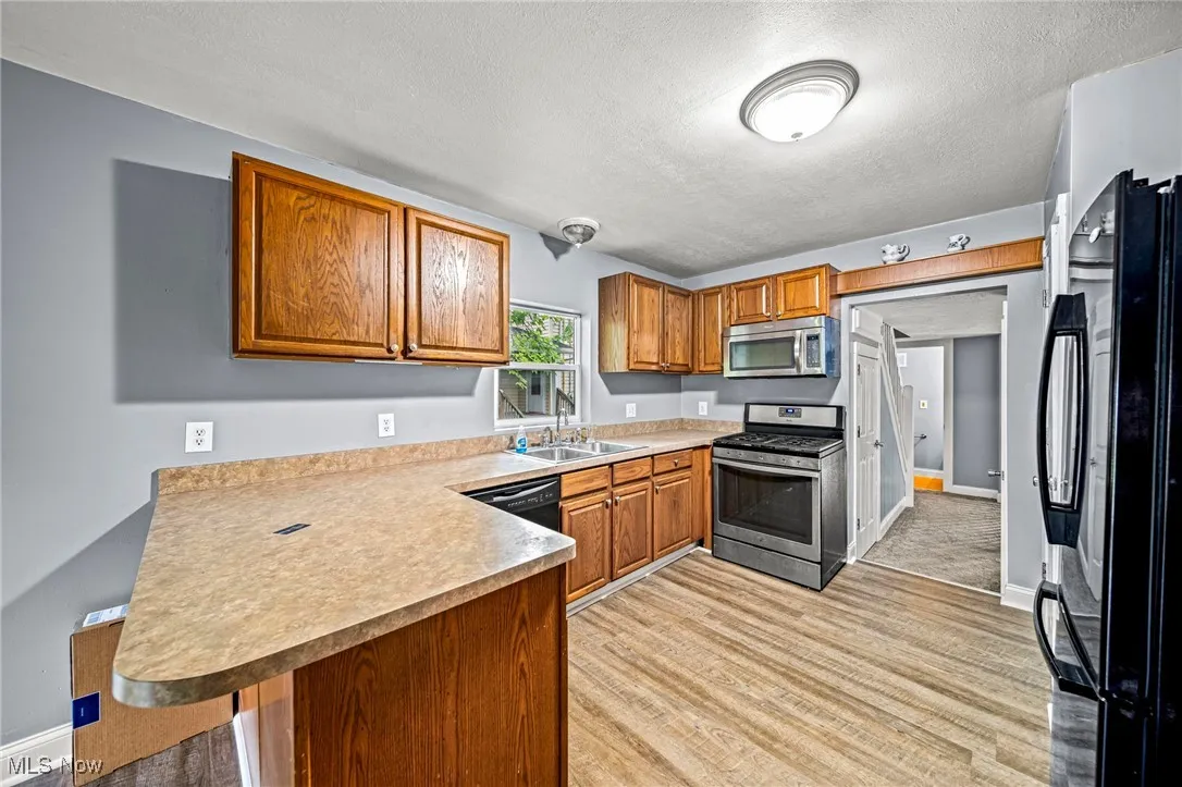 Kitchen with appliances with stainless steel finishes, brown cabinets, a textured ceiling, a peninsula, and light wood-type flooring