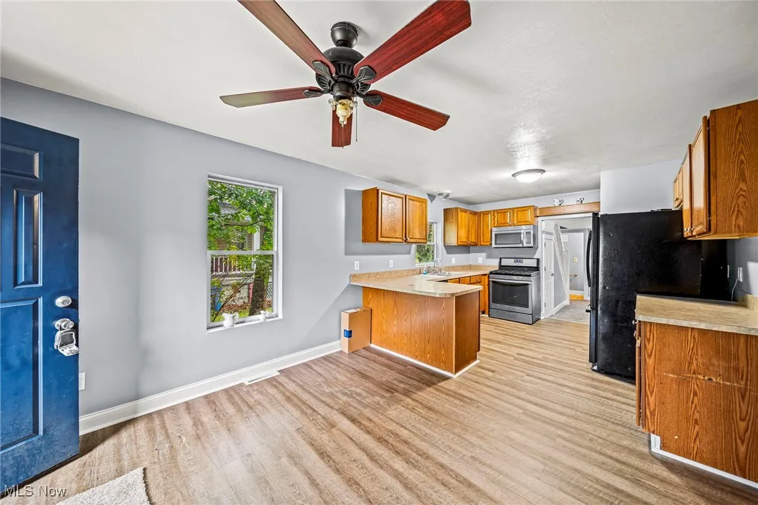 Kitchen with a peninsula, brown cabinetry, light countertops, stainless steel appliances, and light wood-type flooring