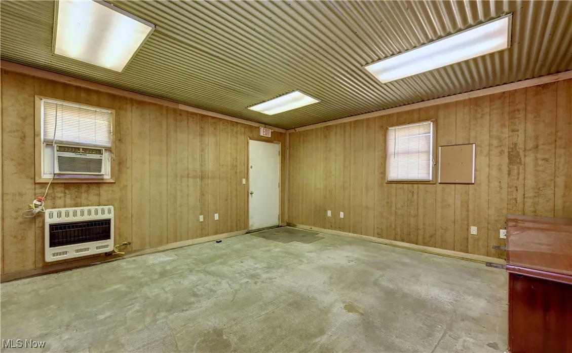 Spare room featuring heating unit, cooling unit, concrete flooring, and wooden walls