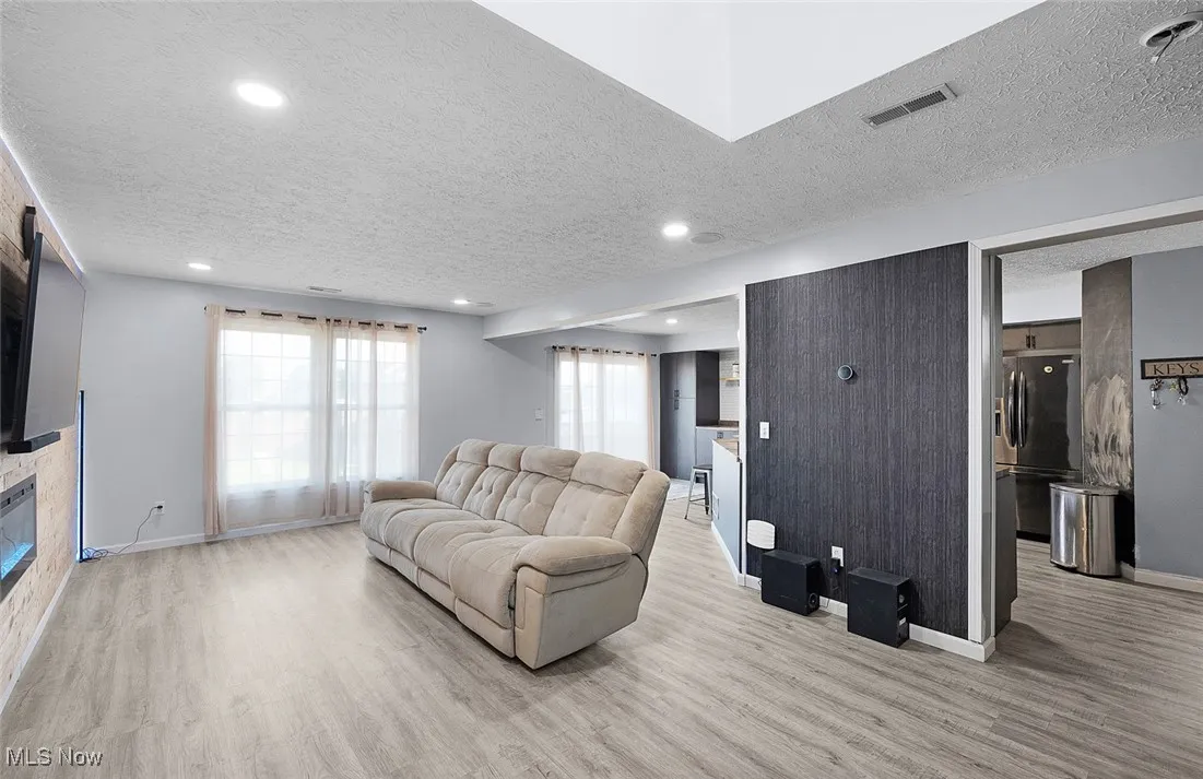 Living room featuring wood finished floors, a textured ceiling, recessed lighting, and a glass covered fireplace