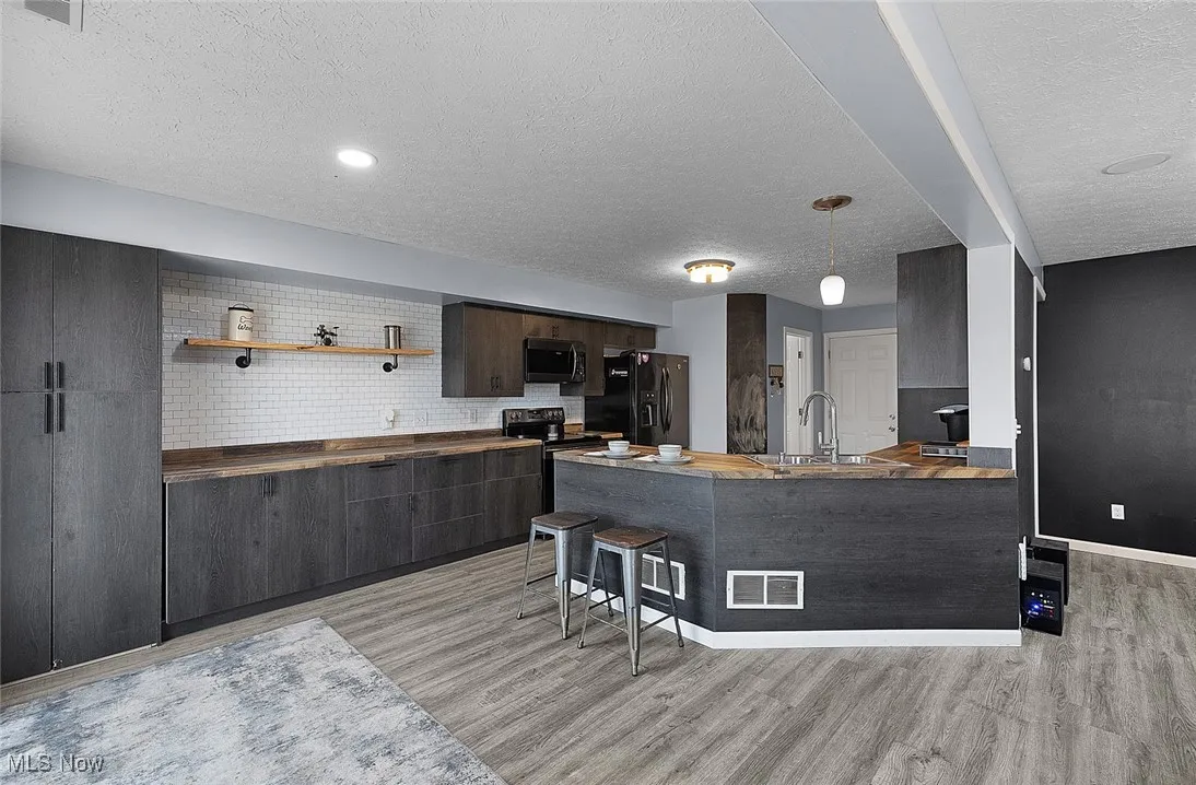 Kitchen featuring black appliances, light wood-style flooring, a textured ceiling, and a peninsula