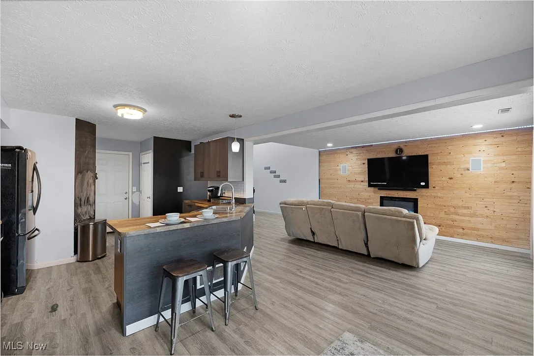 Kitchen featuring light wood finished floors, a breakfast bar, freestanding refrigerator, wooden walls, and a peninsula