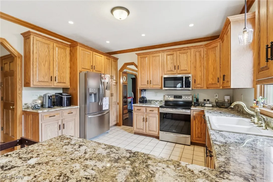 Kitchen with stainless steel appliances, light tile patterned floors, light stone counters, decorative light fixtures, and recessed lighting