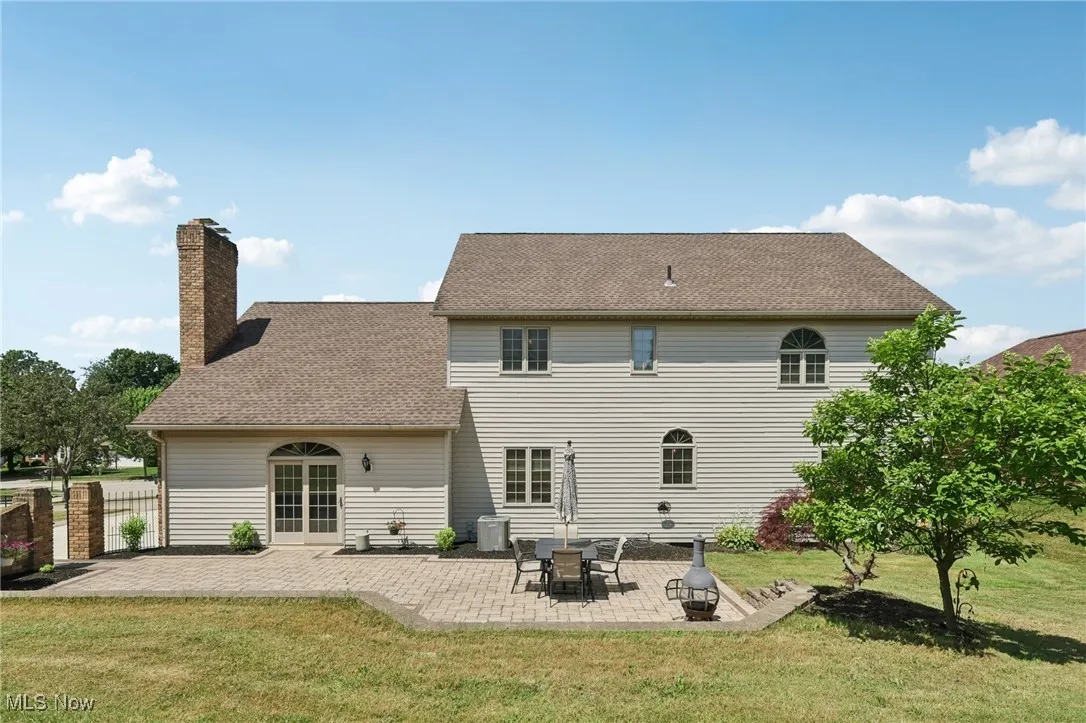 Rear view of house with a chimney, a patio, and roof with shingles