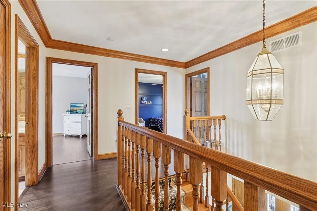 Hallway featuring an upstairs landing, dark wood-type flooring, ornamental molding, and a chandelier