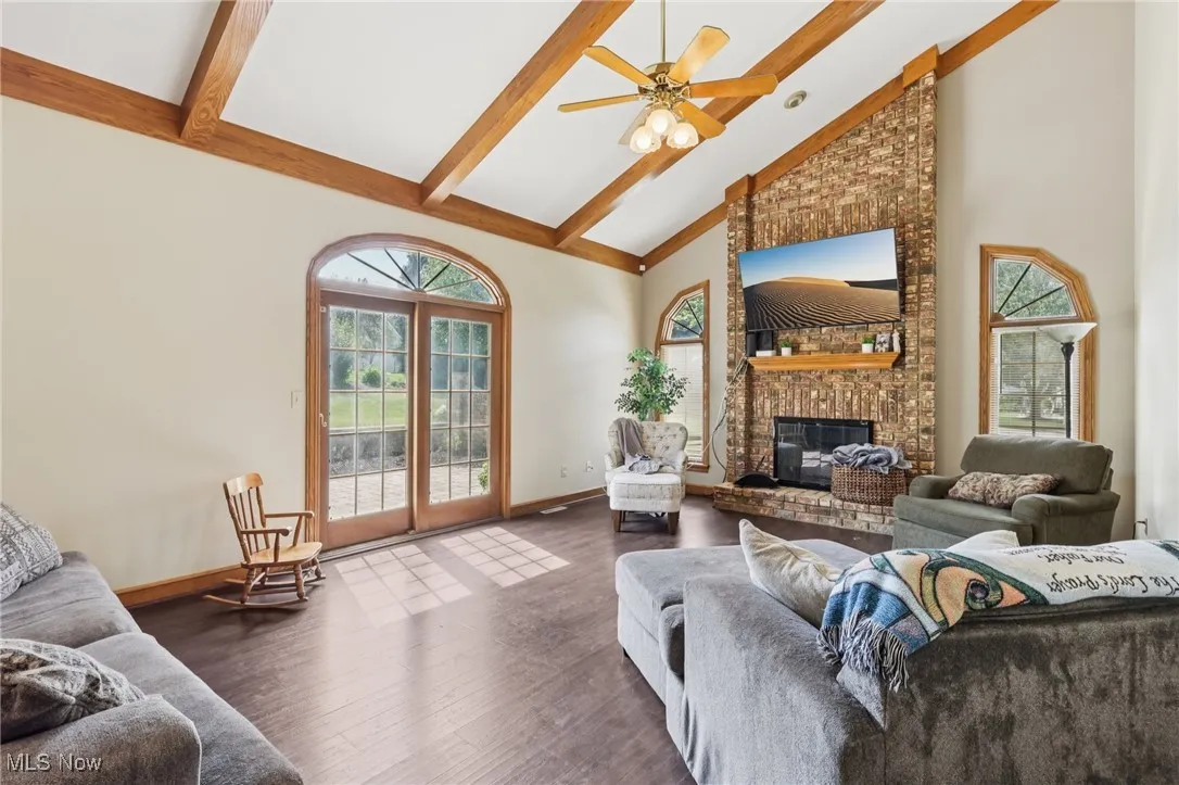 Living room featuring high vaulted ceiling, beamed ceiling, wood finished floors, a fireplace, and a ceiling fan