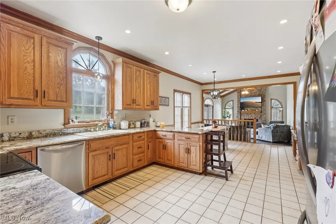 Kitchen with appliances with stainless steel finishes, a peninsula, light tile patterned floors, crown molding, and pendant lighting