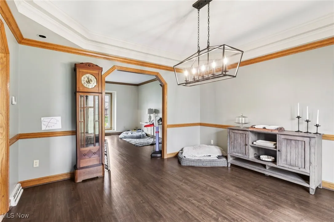 Dining space with crown molding, wood finished floors, arched walkways, a chandelier, and a baseboard heating unit