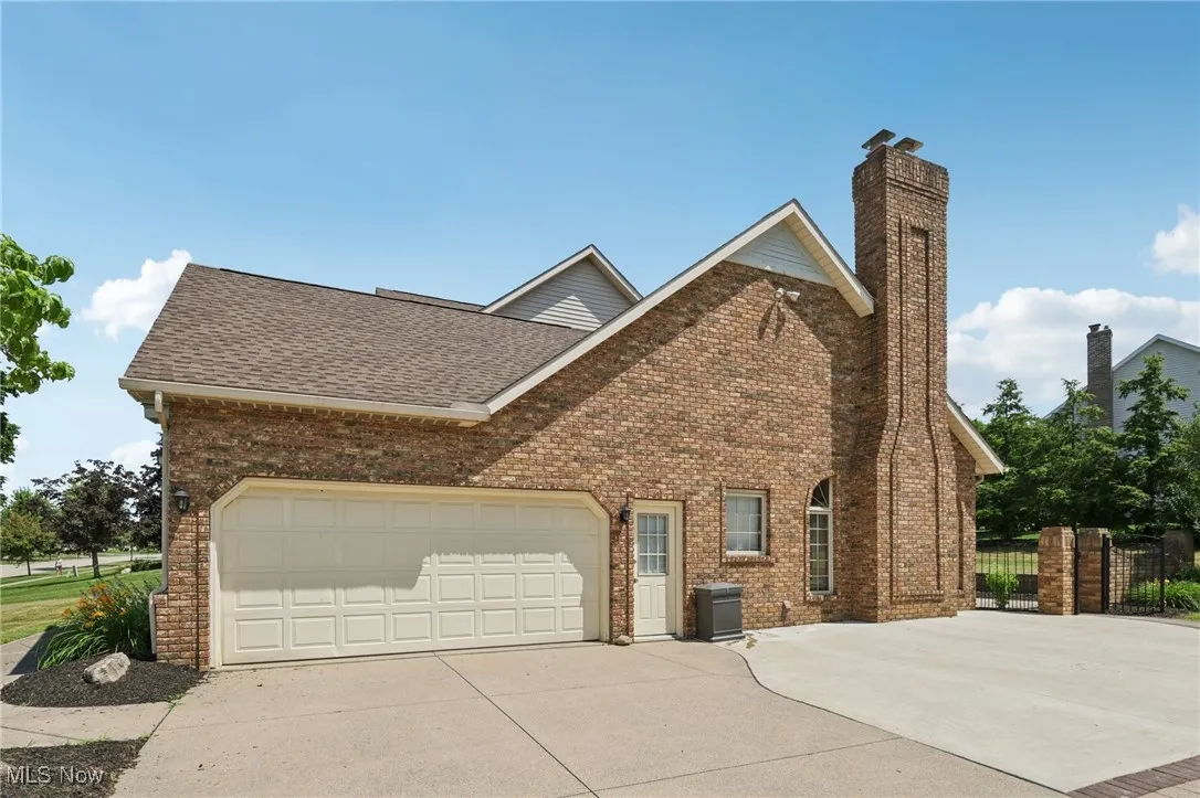 View of side of property with driveway, brick siding, a chimney, and a shingled roof