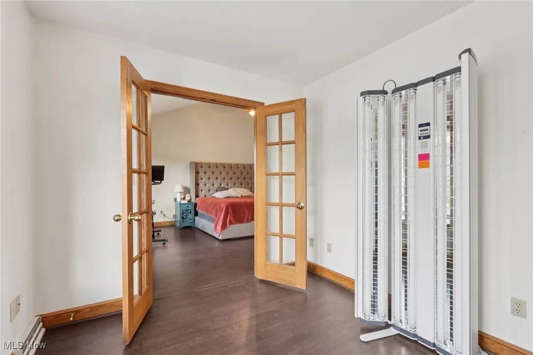 Bedroom with french doors, wood finished floors, and baseboard heating