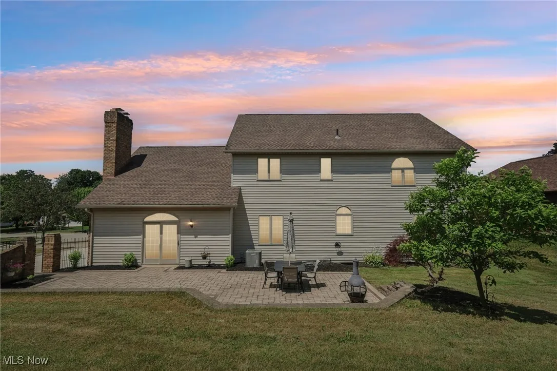 Back of house featuring a patio area, a chimney, and a shingled roof