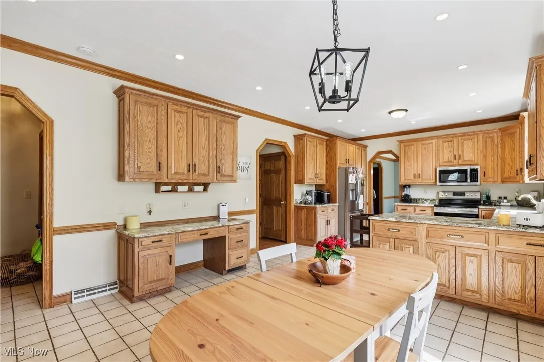 Kitchen featuring appliances with stainless steel finishes, arched walkways, light tile patterned flooring, crown molding, and hanging light fixtures