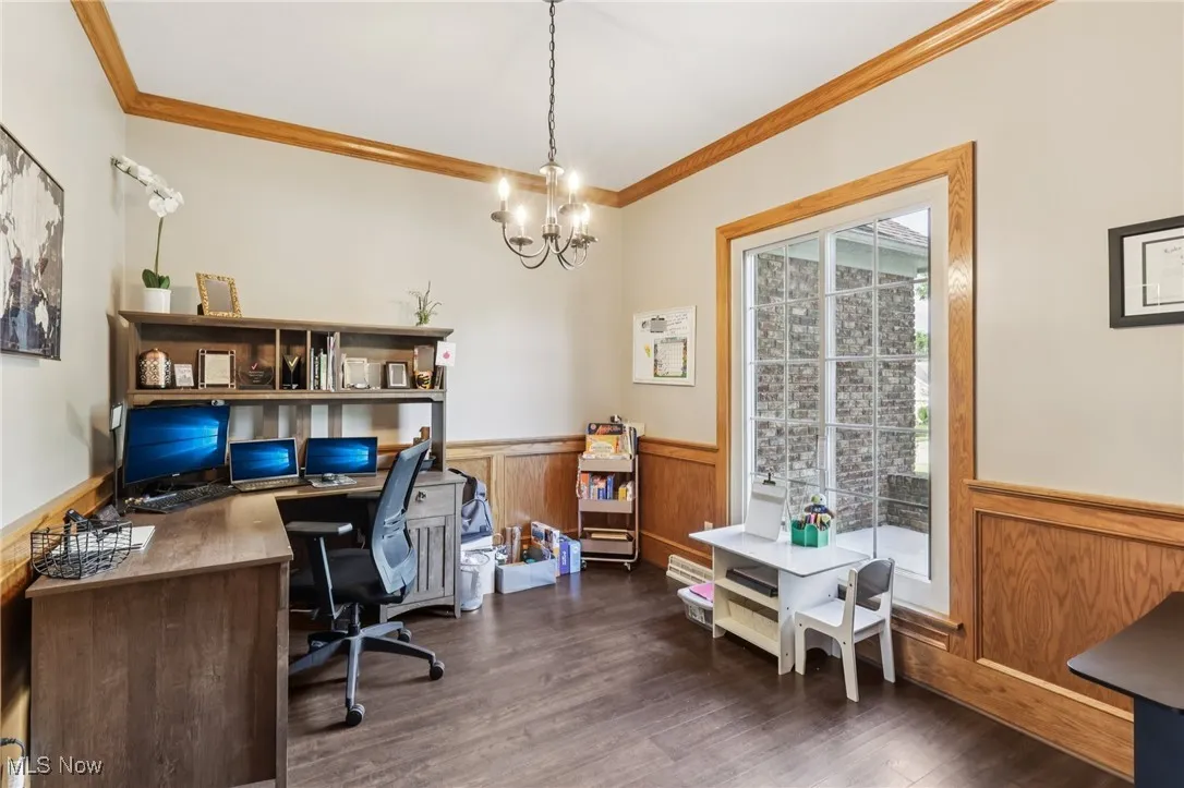 Office space featuring a wainscoted wall, ornamental molding, a chandelier, and dark wood-style flooring
