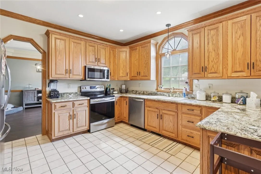Kitchen with appliances with stainless steel finishes, ornamental molding, pendant lighting, light stone counters, and light tile patterned flooring
