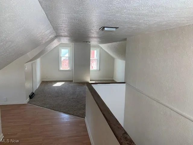 Additional living space featuring a textured ceiling, wood finished floors, a textured wall, and lofted ceiling