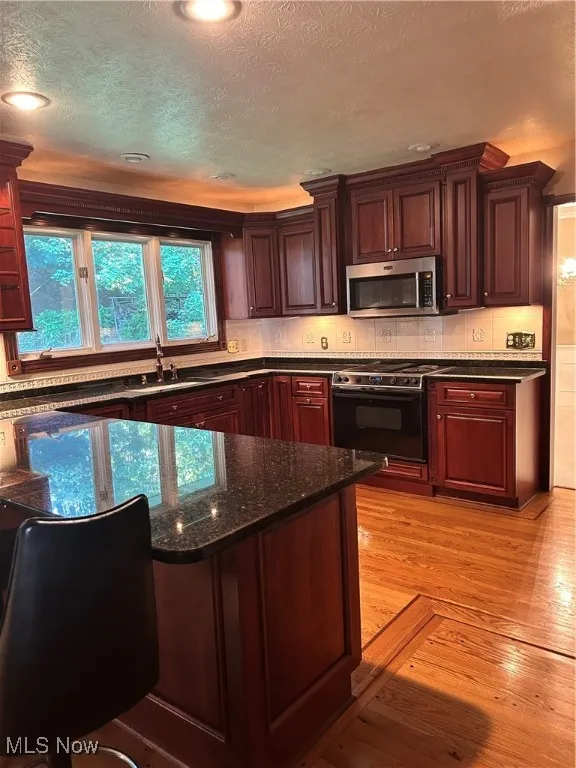 Kitchen with stove, a textured ceiling, dark stone counters, tasteful backsplash, and recessed lighting