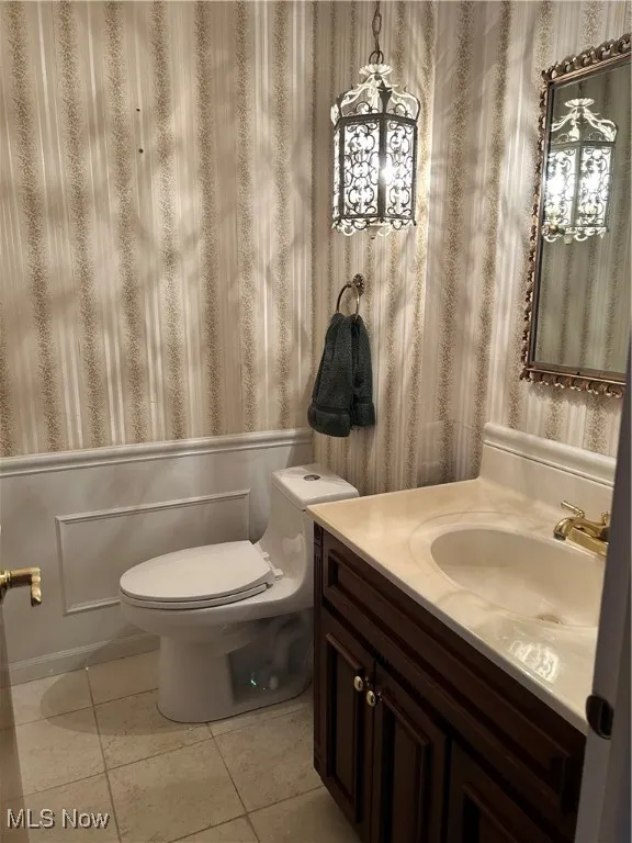 Bathroom featuring wallpapered walls, vanity, tile patterned flooring, and a wainscoted wall