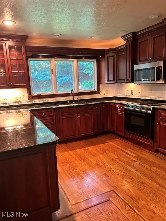 Kitchen featuring range, light wood finished floors, dark stone countertops, glass insert cabinets, and a textured ceiling