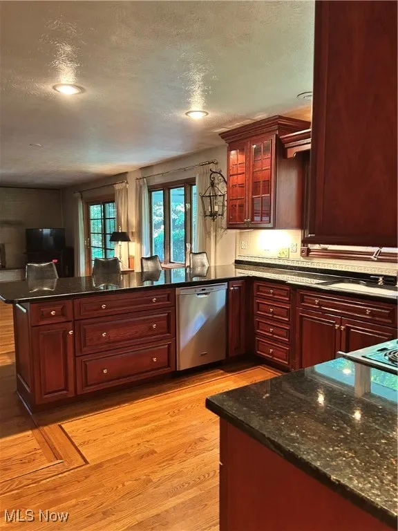 Kitchen featuring dishwashing machine, reddish brown cabinets, light wood-style flooring, a textured ceiling, and a peninsula