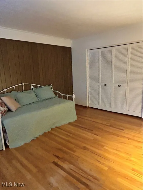 Bedroom with light wood-style flooring, wood walls, and a closet