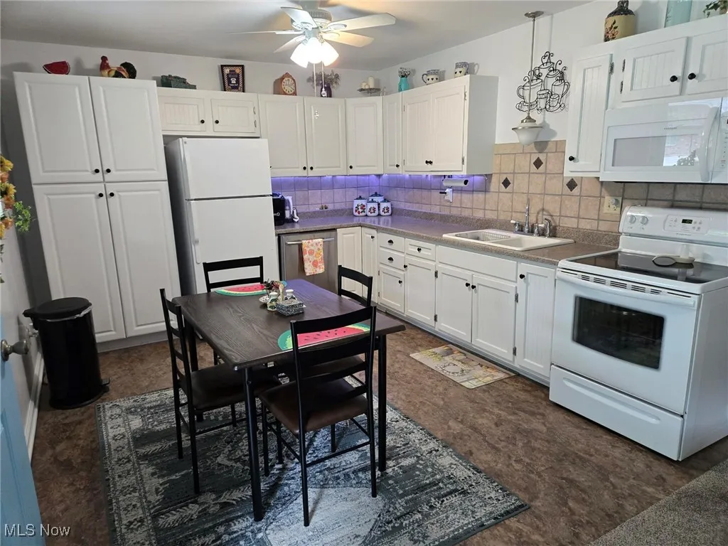 Kitchen with white appliances, white cabinetry, ceiling fan, decorative backsplash, and hanging light fixtures