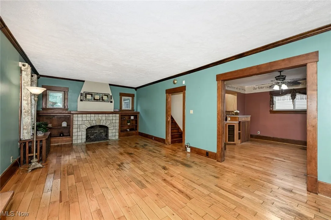 Unfurnished living room with ornamental molding, wood-type flooring, a tiled fireplace, a ceiling fan, and a textured ceiling