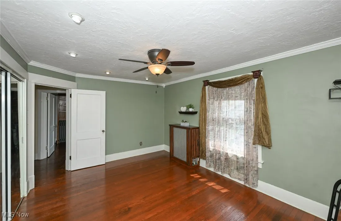 Spare room featuring a ceiling fan, wood finished floors, a textured ceiling, ornamental molding, and a smoke detector