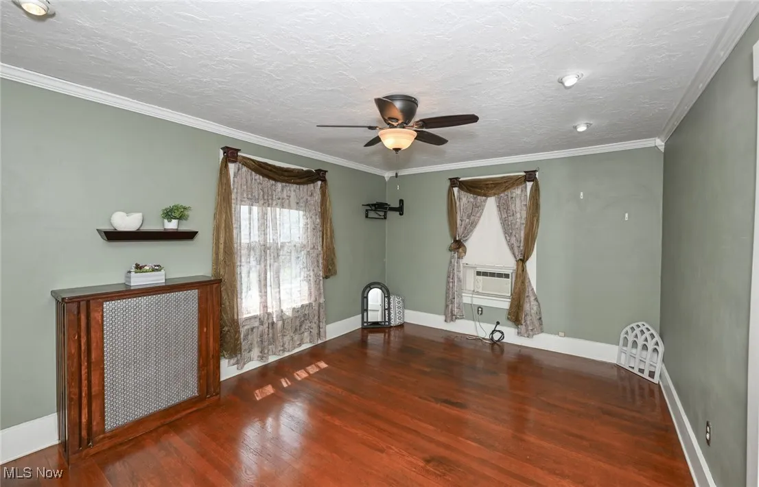 Empty room with wood finished floors, ceiling fan, ornamental molding, a textured ceiling, and cooling unit