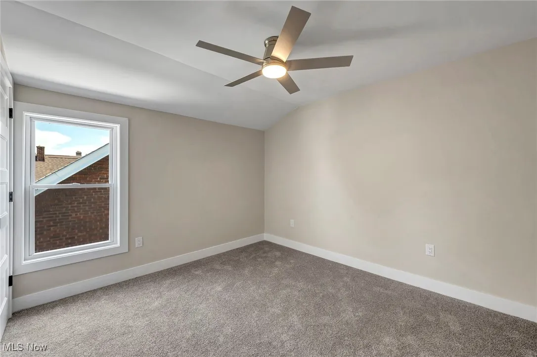 Carpeted empty room with a ceiling fan and lofted ceiling