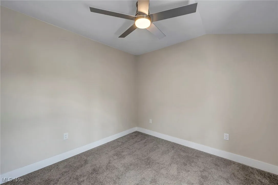 Empty room featuring carpet flooring, ceiling fan, and lofted ceiling