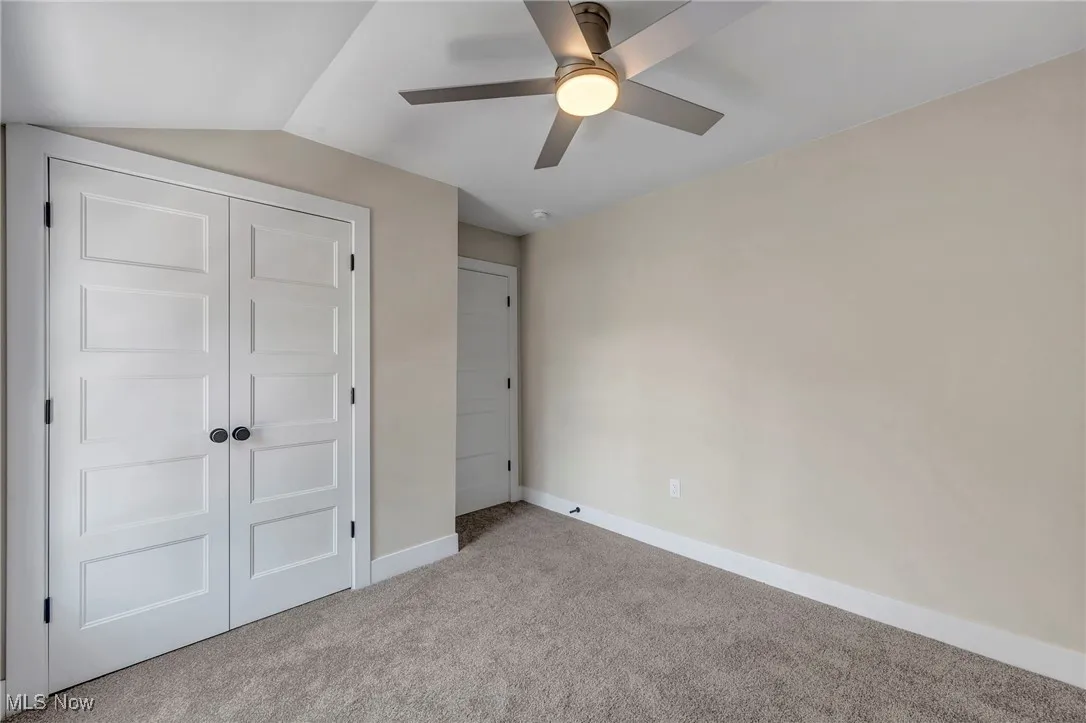 Unfurnished bedroom with carpet flooring, a closet, a ceiling fan, and lofted ceiling