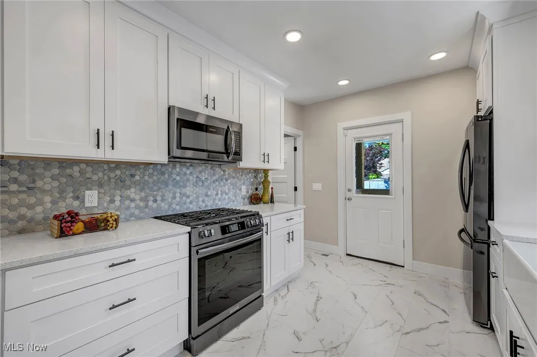 Kitchen with appliances with stainless steel finishes, recessed lighting, tasteful backsplash, white cabinets, and light marble finish flooring