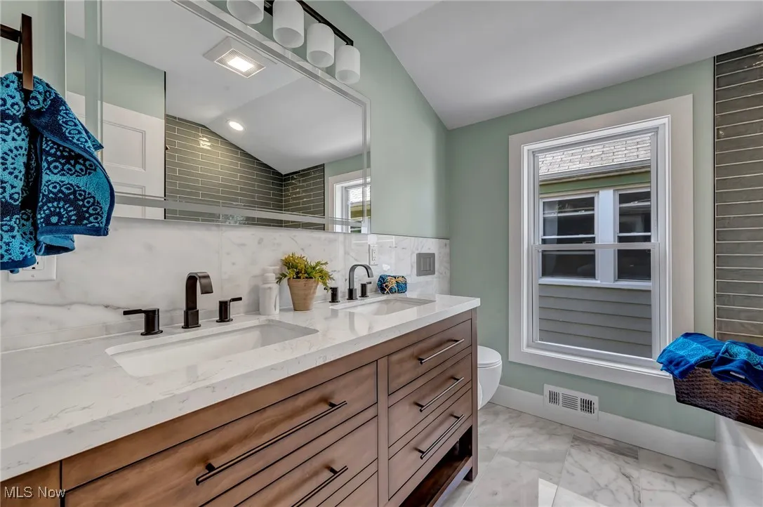 Full bathroom with lofted ceiling, double vanity, tasteful backsplash, and marble finish flooring