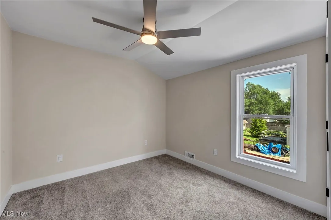 Empty room with light colored carpet, ceiling fan, and lofted ceiling