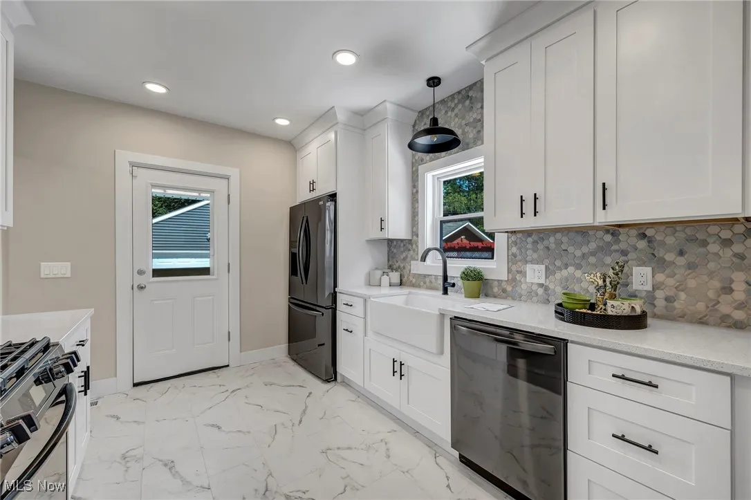 Kitchen featuring dishwasher, black fridge with ice dispenser, stainless steel range with gas stovetop, backsplash, and white cabinetry