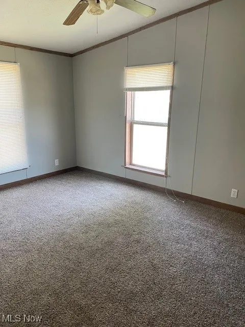 Carpeted empty room with ornamental molding and a ceiling fan