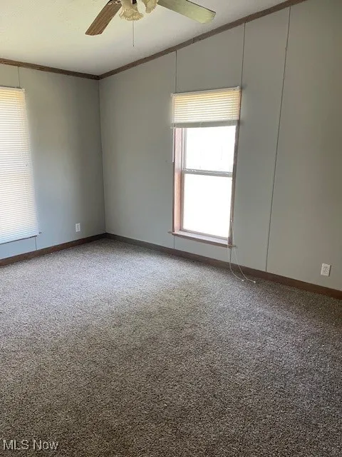 Empty room with crown molding, ceiling fan, carpet flooring, and vaulted ceiling