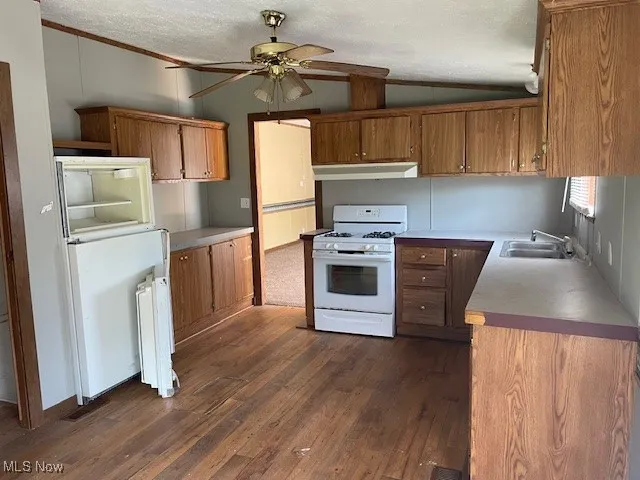 Kitchen with gas range gas stove, under cabinet range hood, brown cabinets, lofted ceiling, and radiator heating unit
