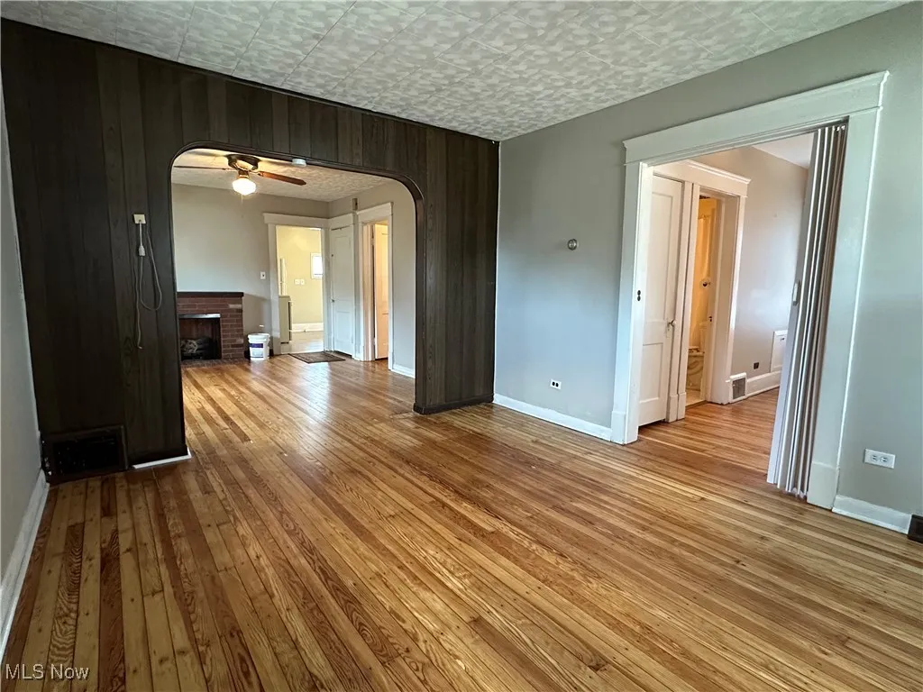Unfurnished room featuring arched walkways, wooden walls, hardwood / wood-style flooring, a brick fireplace, and a ceiling fan