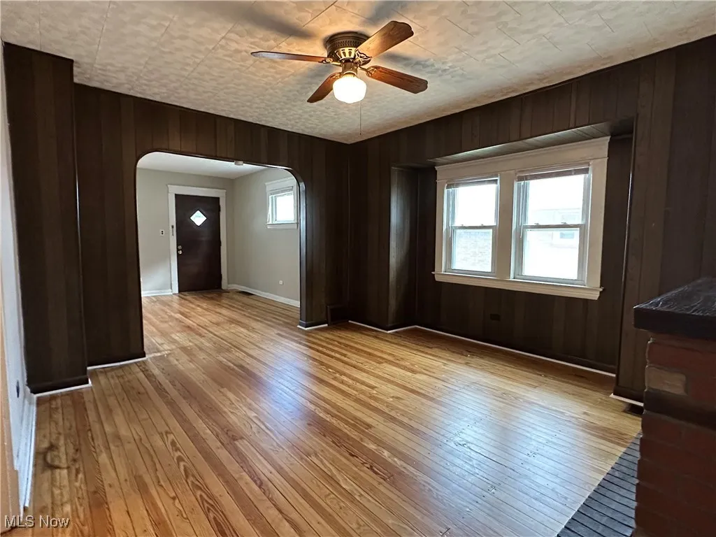 Unfurnished room featuring arched walkways, a ceiling fan, light wood-style floors, and wooden walls