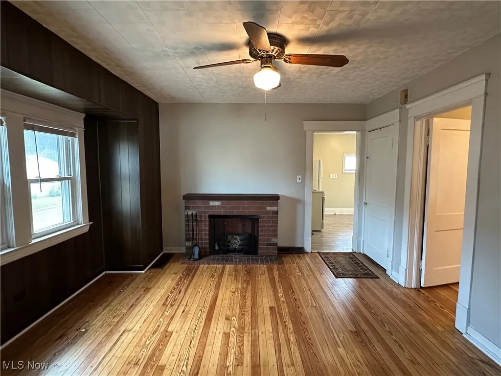 Unfurnished living room featuring hardwood / wood-style floors, a ceiling fan, and a fireplace