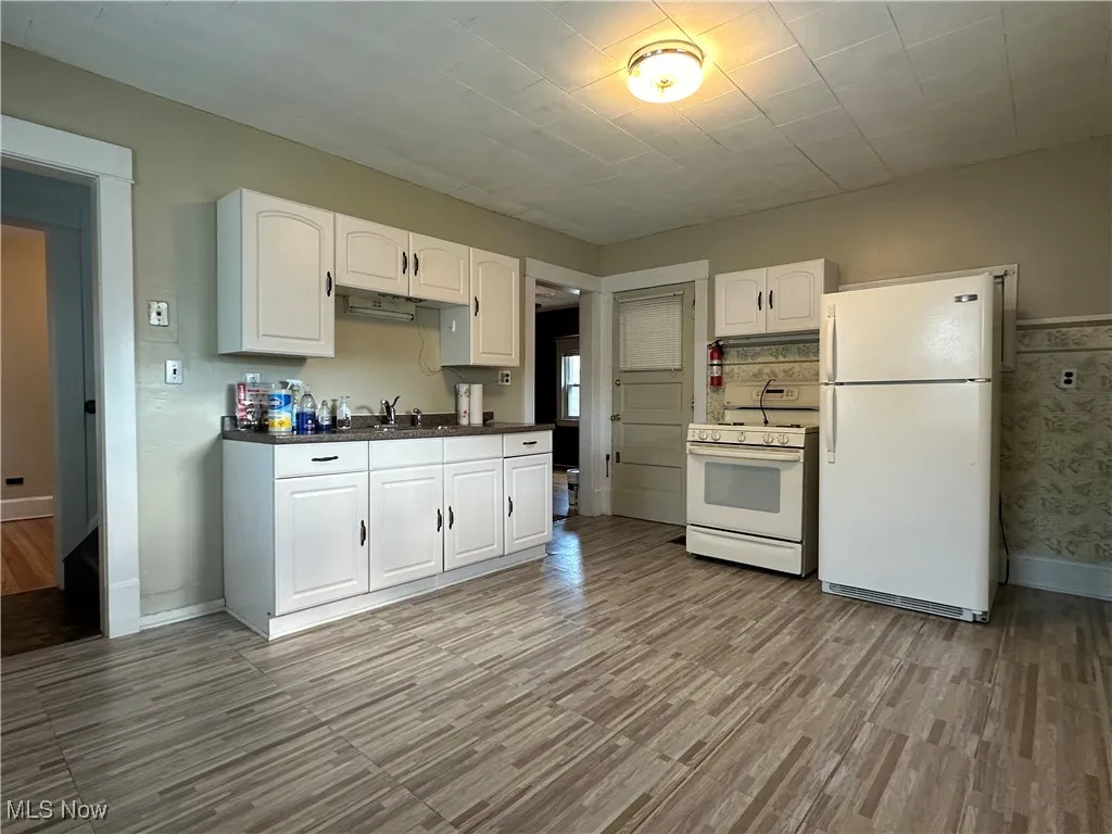Kitchen with white appliances, dark countertops, light wood-style flooring, and white cabinetry