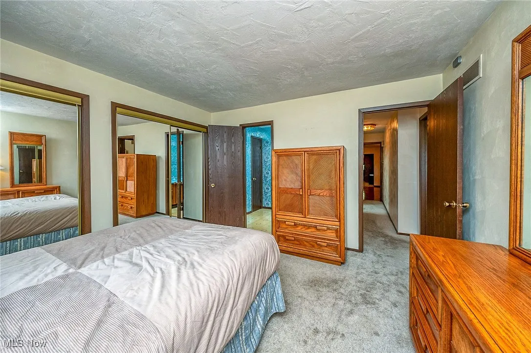 Bedroom featuring light carpet, multiple closets, and a textured ceiling