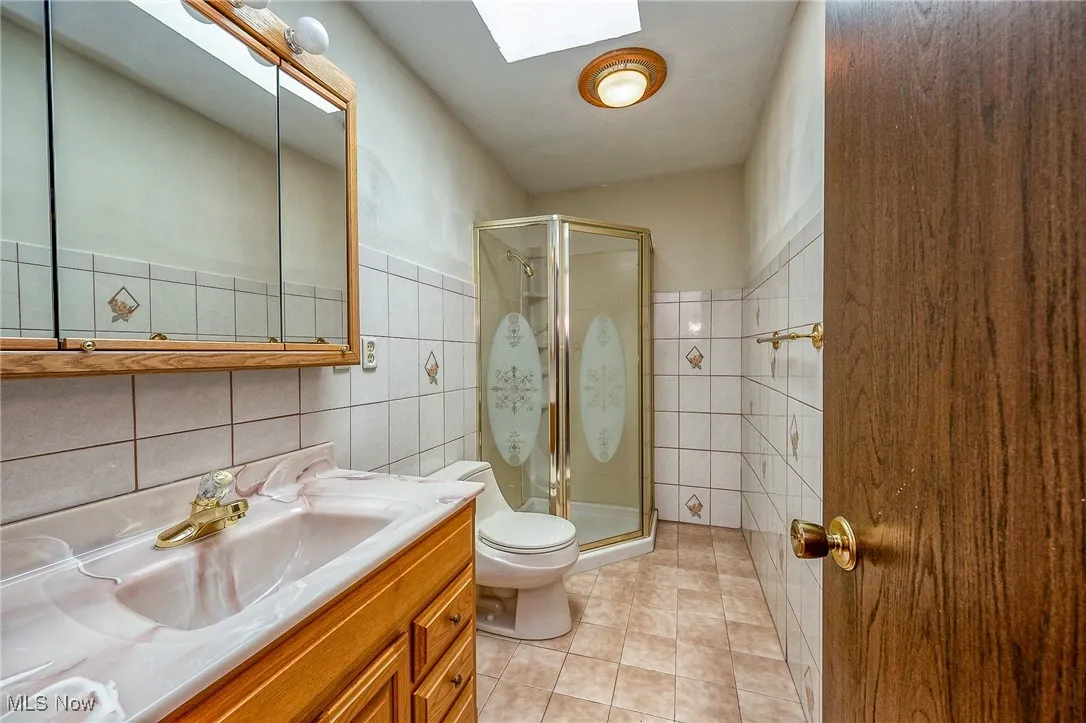 Bathroom featuring tile walls, a skylight, a stall shower, vanity, and tile patterned flooring