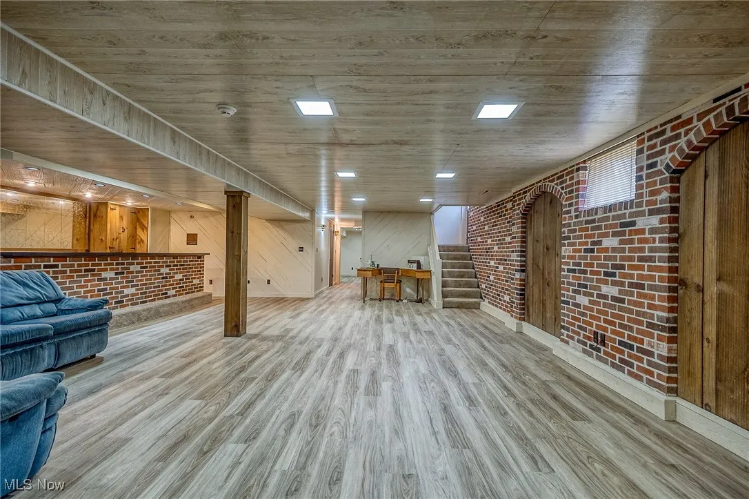 Room featuring brick wall, stairway, wood finished floors, and wood walls