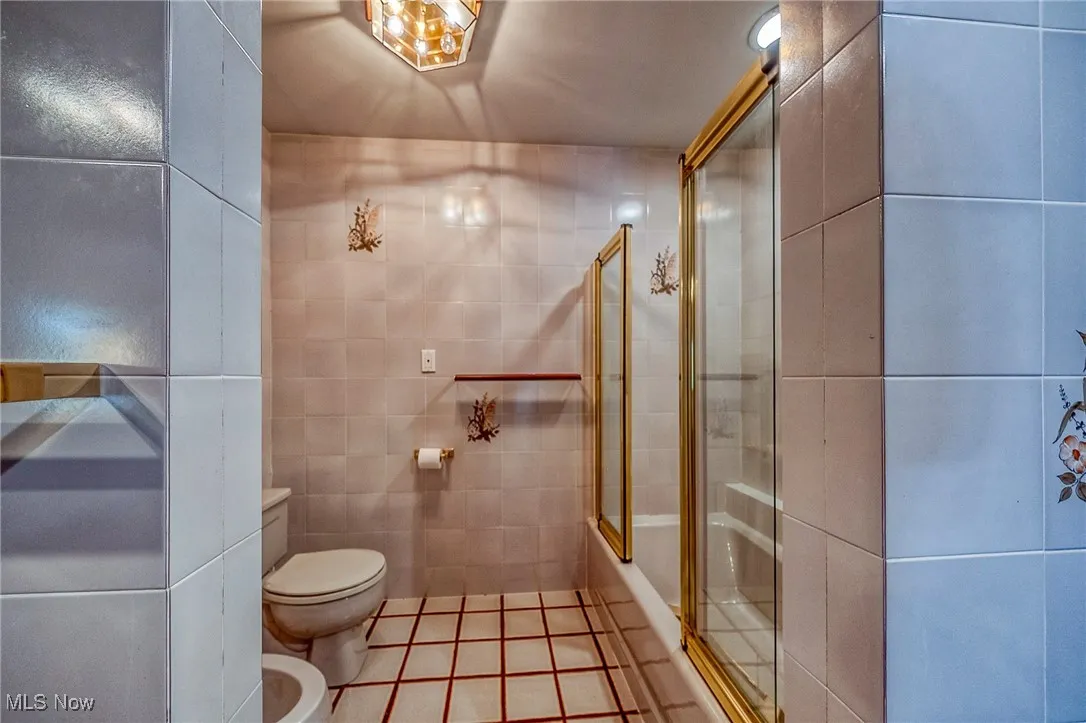 Full bathroom featuring tile walls, tile patterned flooring, a bidet, and bath / shower combo with glass door