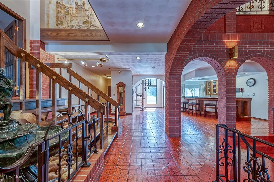 Foyer featuring arched walkways, ornate columns, stairways, and brick wall